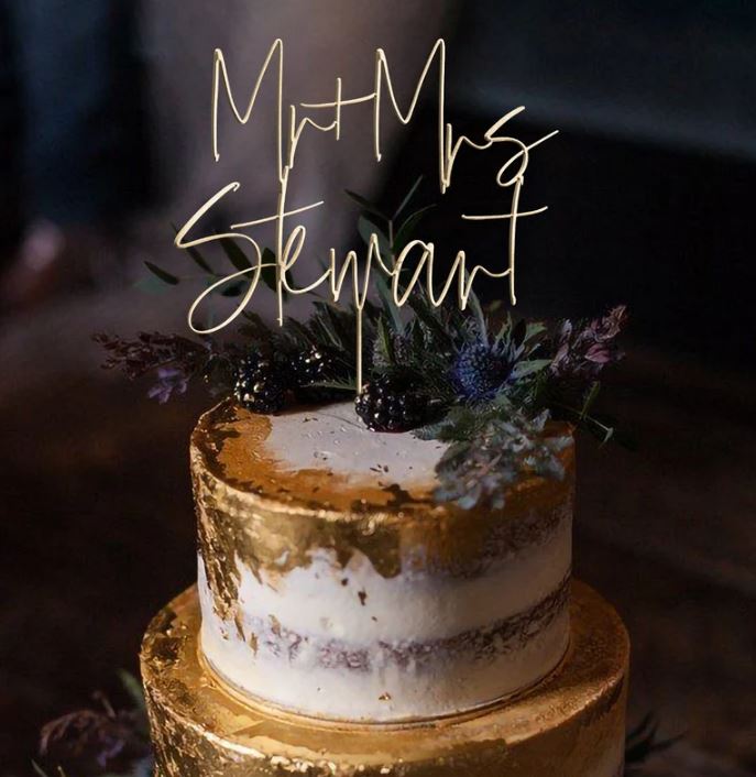 Two-tier wedding cake with a gold leaf finish topped with fresh blackberries, thistle, and lavender, with a gold wire Mr and Mrs Stewart calligraphy topper
