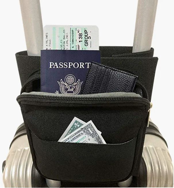 Black luggage handle caddy organizer holding a passport, boarding pass, wallet, and cash mounted on a silver rolling suitcase handle